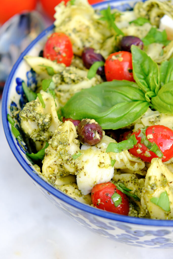 Tortellini pesto salad in a blue serving bowl topped with red tomatoes. 