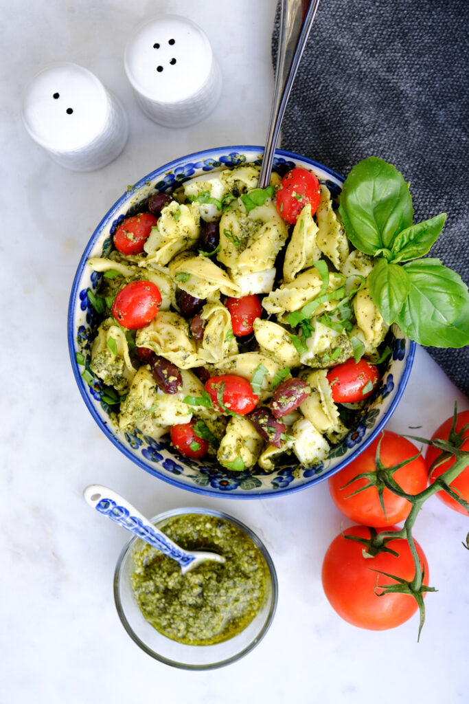 Top view of tortellini pasta salad in a blue bowl with pesto on the side. 