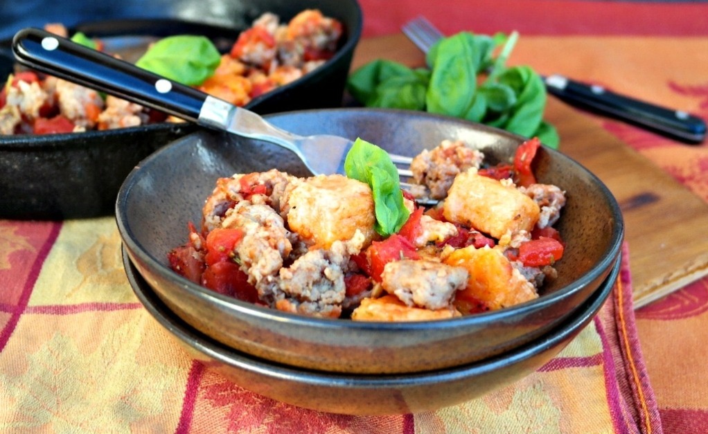 Homemade sweet potato gnocchi with sausage in brown serving bowls. 