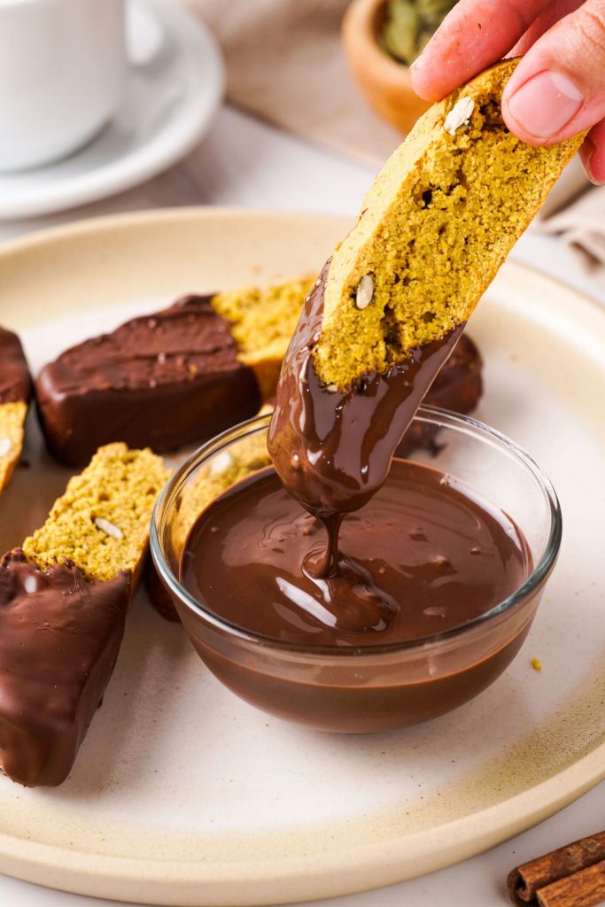 Small bowl with melted chocolate and a biscotti dipped in it. 