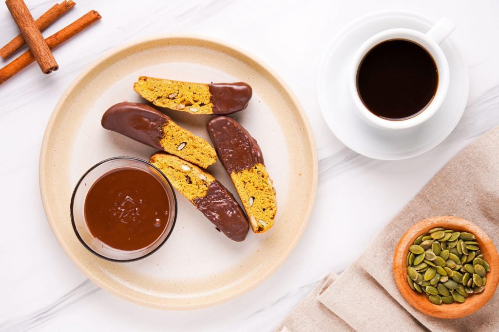 Biscotti dipped in chocolate on a plate with coffee on the side. 