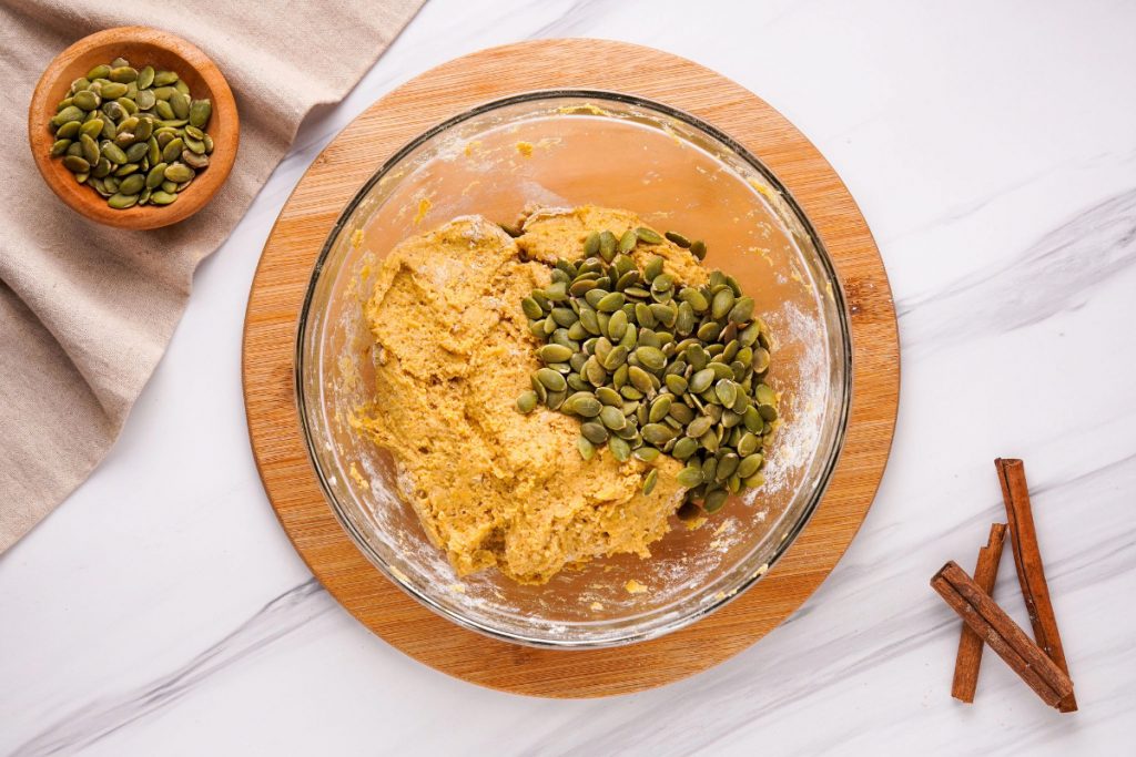 Wet and dry ingredients in a mixing bowl with pumpkin seeds.