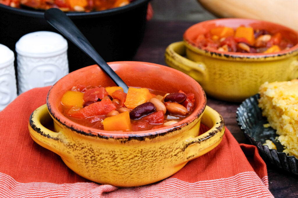 Yellow bowls filled with chili with a slice of cornbread on the side. 