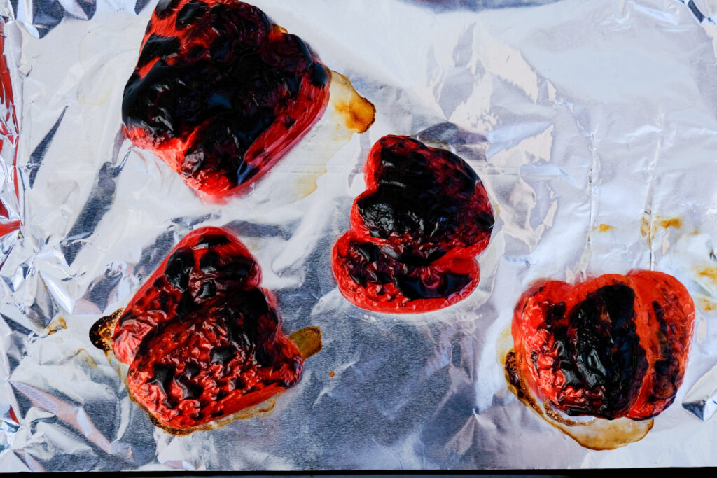 Blackened red bell peppers on a foil lined baking sheet. 