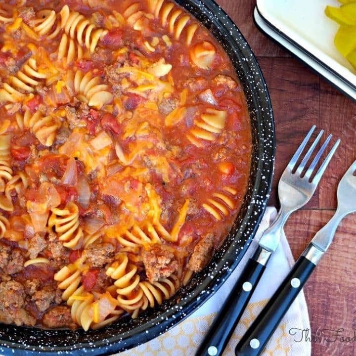 Cheeseburger Pasta Skillet meal in a black pan with pickles on the side