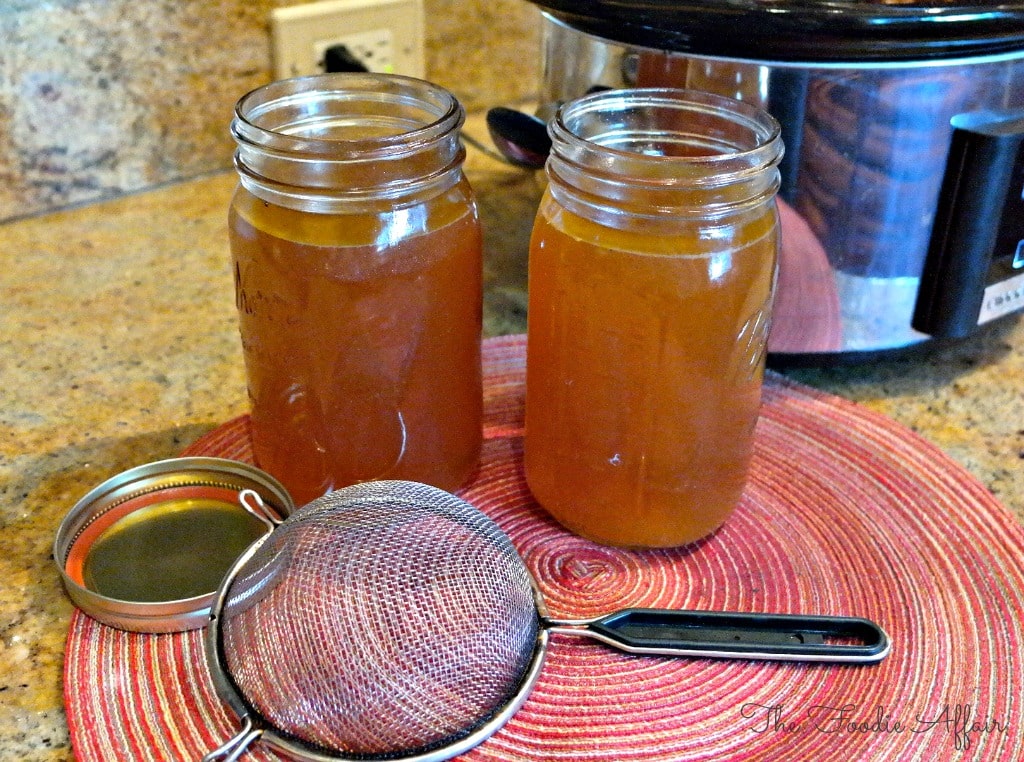 Homemade Slow Cooker Turkey Stock in mason jars with a strainer on the side