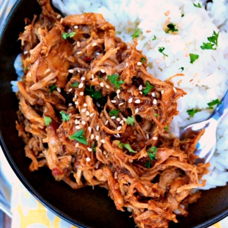 Shredded chicken topped with sesame and green onions on a plate with rice.