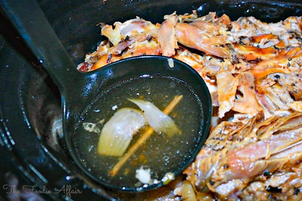 Turkey stock in a slow cooker simmering with a soup spoon scooping up the broth. 