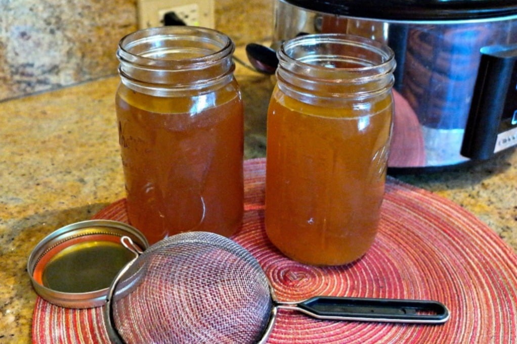 Slow cooker turkey stock in mason jars with a strainer on the side of the jars. 