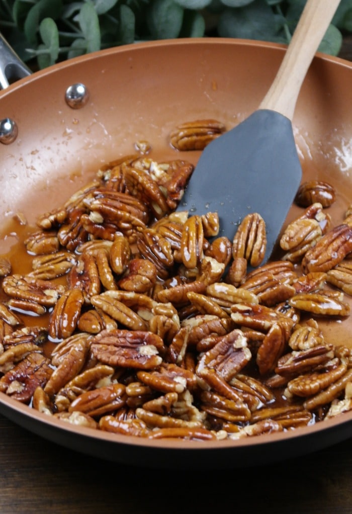 Rubber spatula stirring pecans in maple syrup to carmelize. 