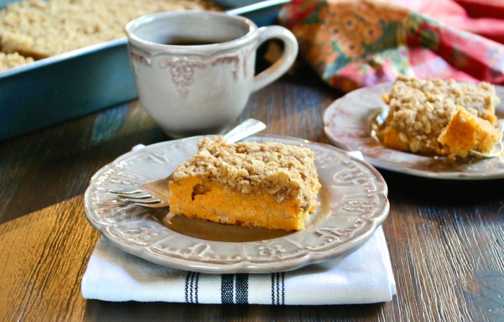 Crumble cake made with sweet potatoes on a tan plate with a cup of coffee on the side. 