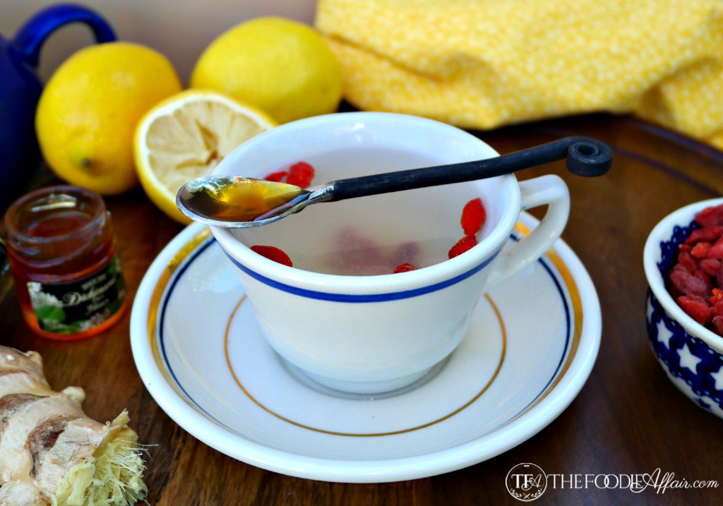 White teacup with blue rim of lemon ginger detox tea with a spoonful of honey