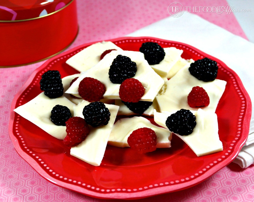 homemade white chocolate bark on a red plate topped with raspberries and blueberries
