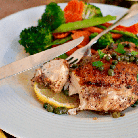 Citrus Chicken Piccata on a white dinner plate with fresh vegetables