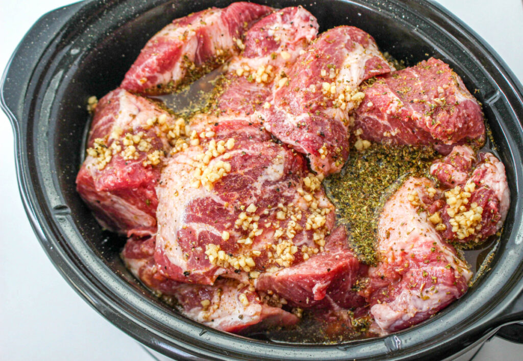 Diced pork in a slow cooker with seasoning before cooking. 