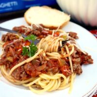 Spaghetti topped with meat sauce on a white plate