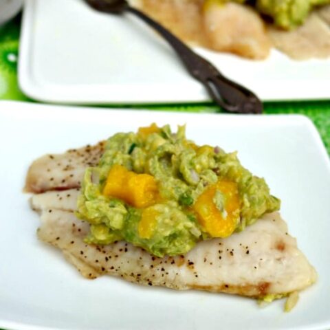 Tilapia fish topped with avocado and mango on a white plate