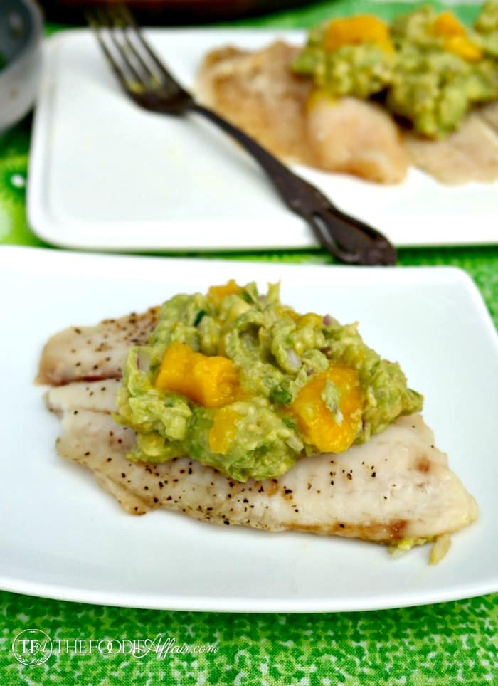 Tilapia fish topped with avocado and mango on a white plate