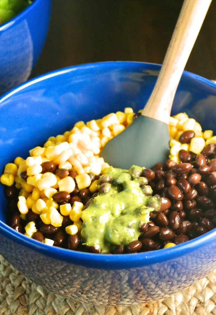 In a blue bowl mixing corn and black beans with cilantro dressing