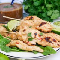 Chicken satay on a white serving dish with peanut sauce on the side.