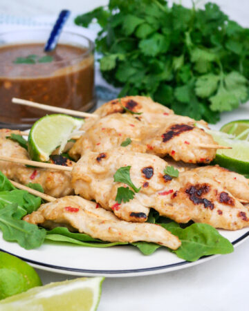Chicken satay on a white serving dish with peanut sauce on the side.