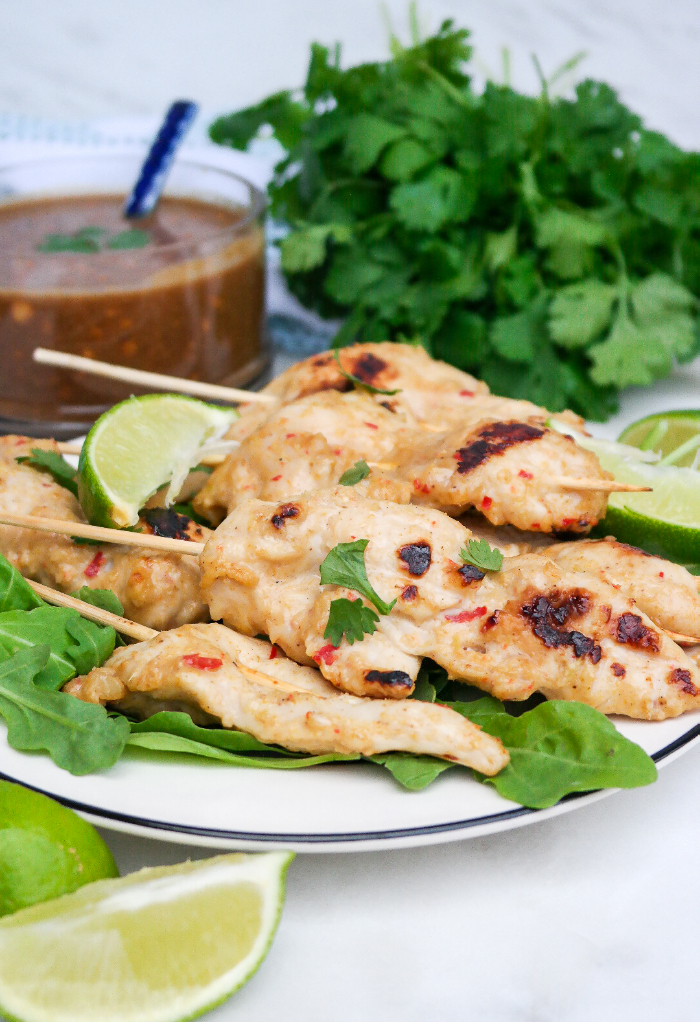 Chicken satay on a white serving dish with peanut sauce on the side. 