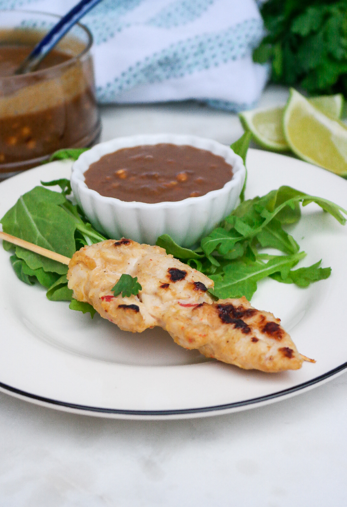 Chicken satay on a white plate with a small bowl of peanut sauce on the side. 
