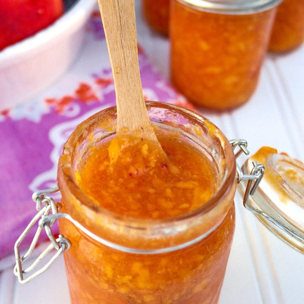 Homemade low sugar peach jam in a mason jar with a wooden spoon.