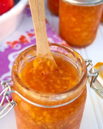 Homemade low sugar peach jam in a mason jar with a wooden spoon.