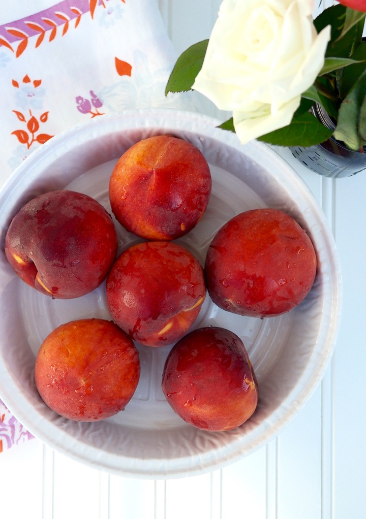 Fresh whole peaches in a white bowl. 