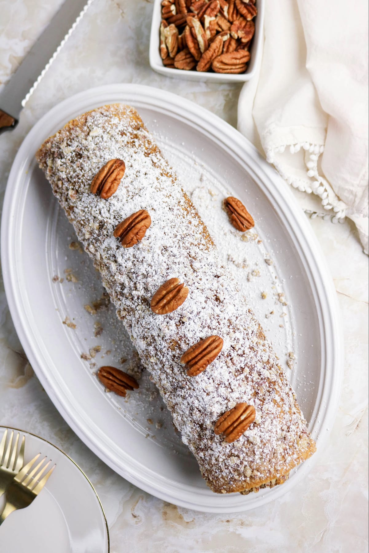 Pumpkin Roll cake on a white platter topped with pecans and powdered sugar.