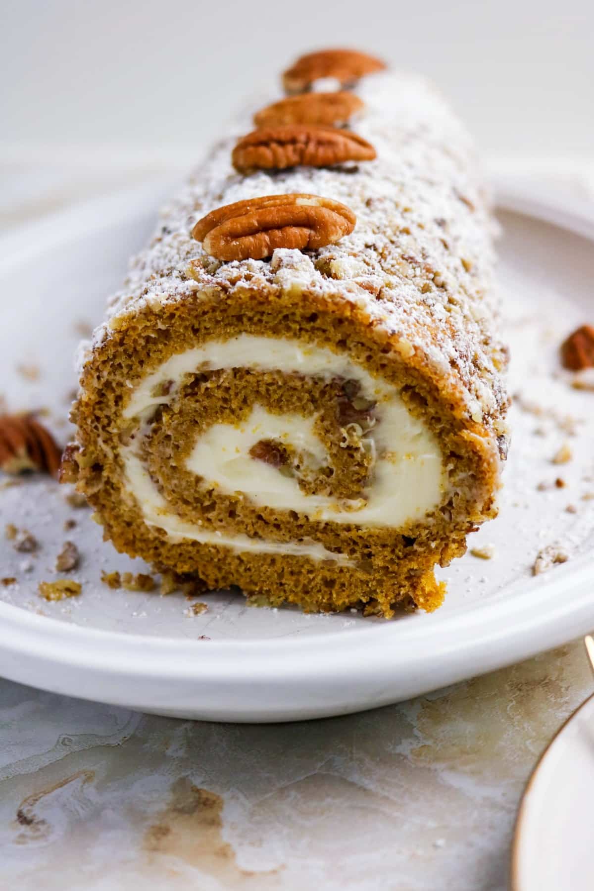 Rolled cake with pumpkin topped with pecan slices.