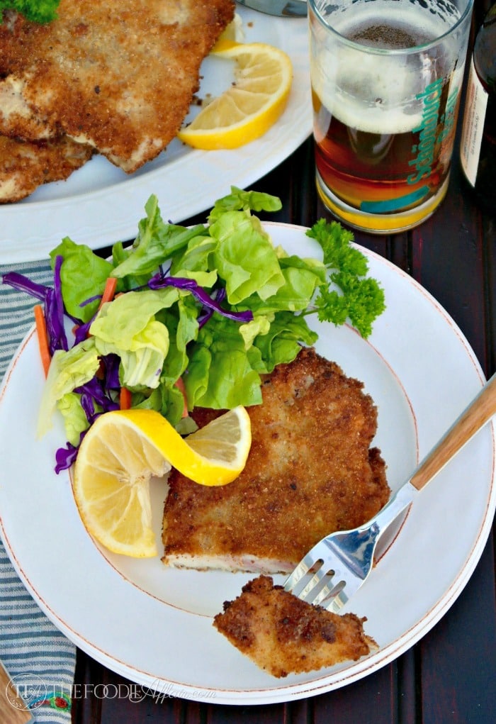 Easy Pork Schnitzel recipe on a white plate with salad and glass of beer on the side