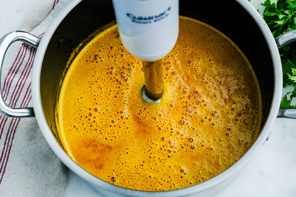 An immersion blender in a Dutch oven blending soft carrots. 