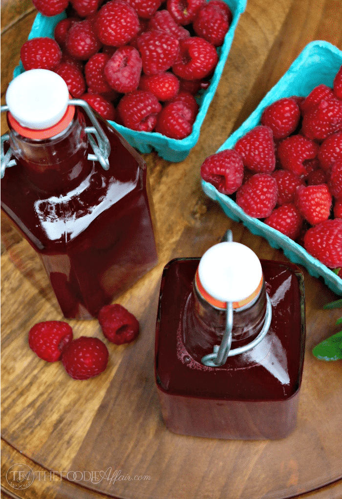 homemade raspberry syrup on a wood tray with bright red fresh berries
