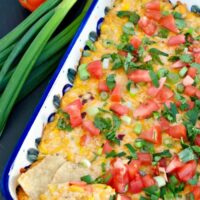 Corn dip in a casserole dish topped with diced tomatoes and onions