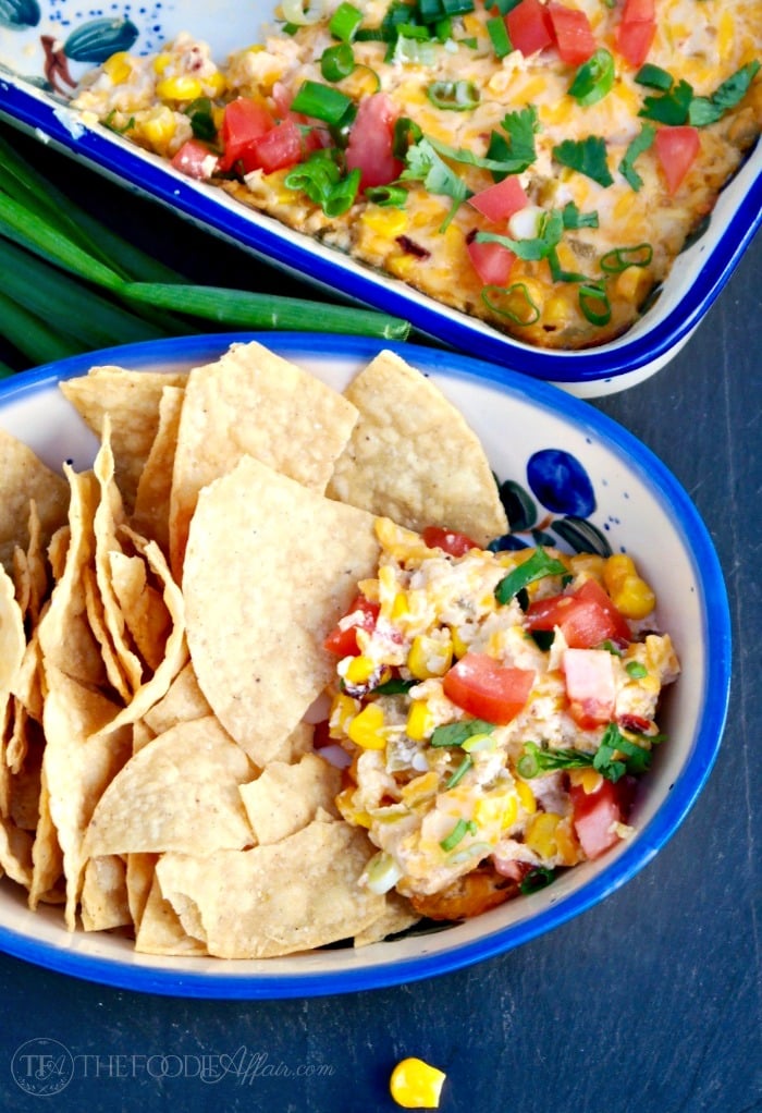 A blue rimmed bowl with corn dip and a side of tortilla chips
