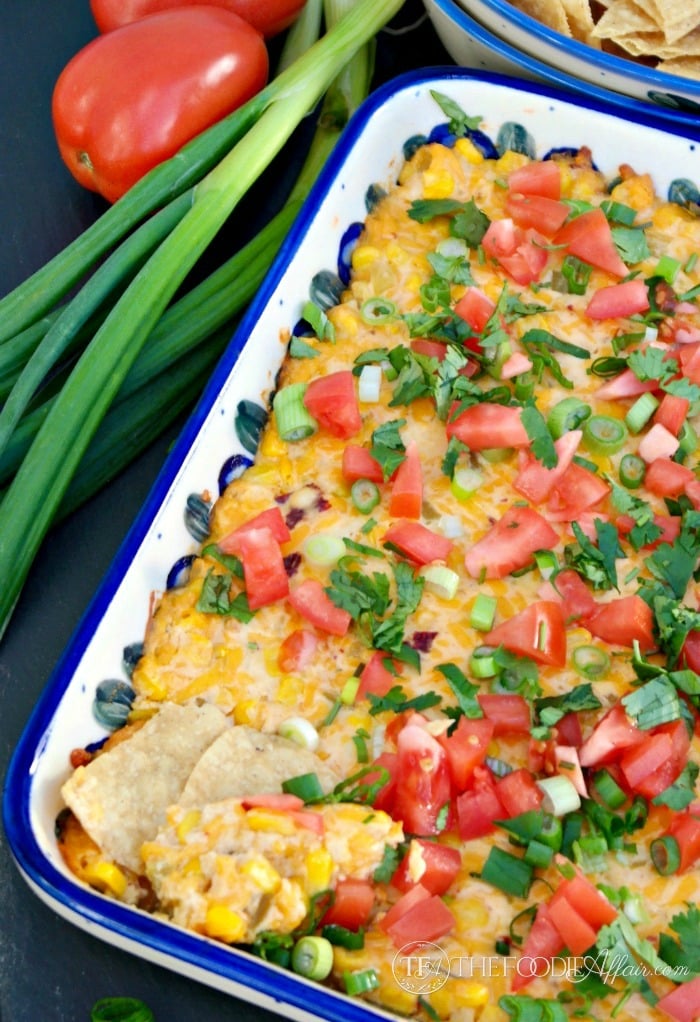 Corn dip in a casserole dish topped with diced tomatoes and onions