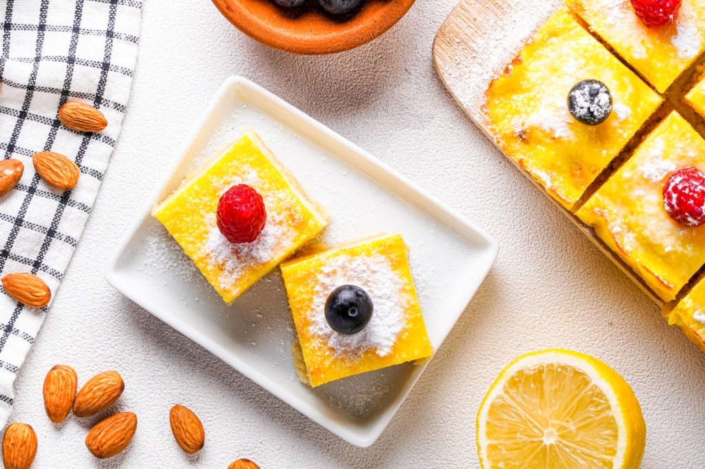 Top view of keto lemon bars on a white square serving dish topped with a raspberry and blueberry.