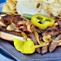 plate with steak sandwich topped with peppers and melted cheese.