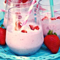 Bright pink smoothie with strawberries and coconut flakes in a clear glass