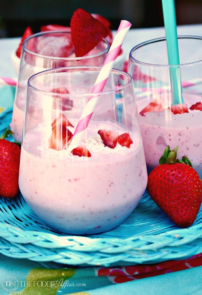 Bright pink smoothie with strawberries and coconut flakes in a clear glass