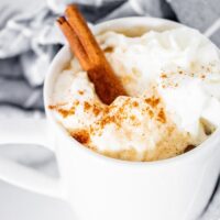 A white mug with coffee topped with whipped cream.