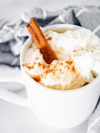 A white mug with coffee topped with whipped cream.