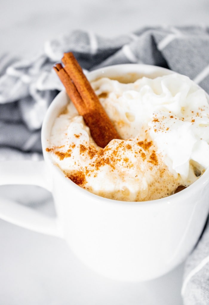 A white mug with coffee topped with whipped cream.