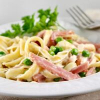 Fettuccini Alfredo with Ham & Peas in a white serving bowl