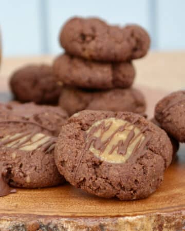 Chocolate keto thumbprint cookies with caramel filling on a wood platter.