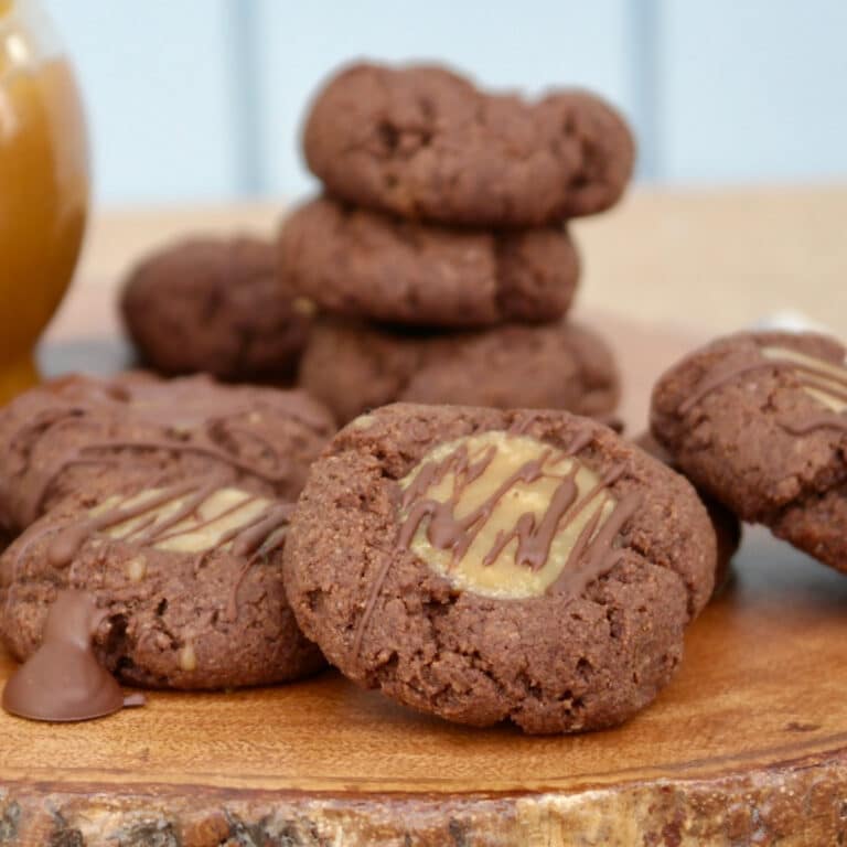 Chocolate keto thumbprint cookies with caramel filling on a wood platter.