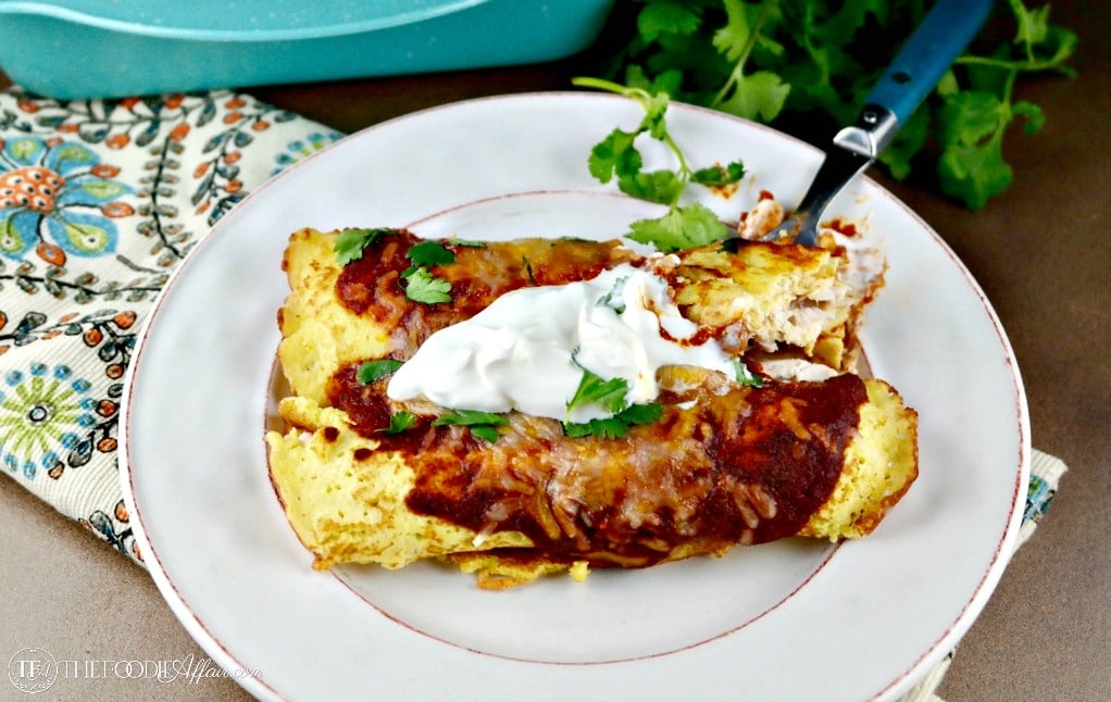 Two low carb enchiladas topped with sour cream and fresh cilantro on a white plate #enchilada #chicken #lowcarb | www.thefoodieaffair.com
