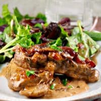 skillet pork chops topped with caramelized onions and bacon on a white plate